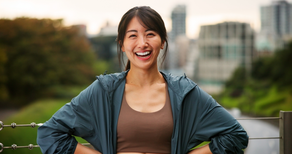 City, fitness and portrait of woman laughing outdoor for cardio or marathon training routine. Bridge, exercise and smile of funny sports athlete or runner in Japan for challenge, health or wellness