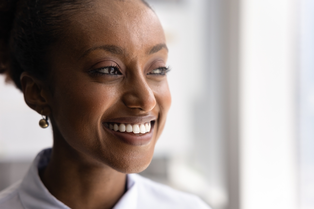 Face close up of happy thoughtful young African American woman, smiling, showing white teeth, thinking, looking at copy space away. Beautiful businesswoman facial closeup
